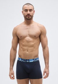Sinivalkoiset ja mustat bokserit, joissa on leveä joustava vyötärönauha, jossa lukee "JACK & JONES" kontrastiväreillä. Pehmeä kangas.