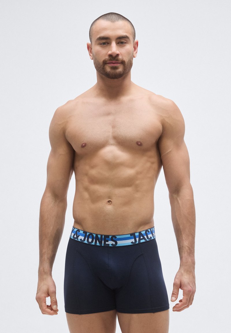 Sinivalkoiset ja mustat bokserit, joissa on leveä joustava vyötärönauha, jossa lukee "JACK & JONES" kontrastiväreillä. Pehmeä kangas.
