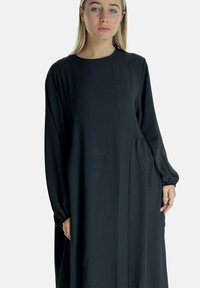 Sort langærmet kjole med rund halsudskæring; lavet af raffineret stof; har en sidelomme og en flydende silhuet.