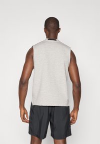 T-shirt sans manches gris en mélange de coton, avec un col rond rehaussé de noir. Associé à un short de sport noir.