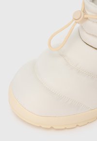 Bežīgi pildīti ziemas zābaki ar biezu zoli un regulējamu auklu aizdari uz baltā fona.