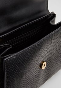 Svart läderhandväska med en texturerad skinnliknande mönster, med ett guldknappslut och flera inre fack.