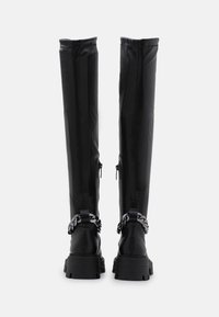 Botas negras hasta la rodilla hechas de cuero suave, con una suela gruesa y acentos de cadena alrededor del tobillo, con cierres de cremallera en el lateral.