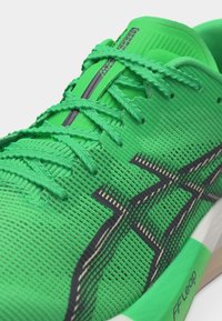 Φωτεινό πράσινο αθλητικό παπούτσι με μαύρες λωρίδες λογότυπου, λεπτομερή ύφανση, κορδόνια στο ίδιο χρώμα και το κείμενο "MAGIC SPEED" στη γλώσσα.