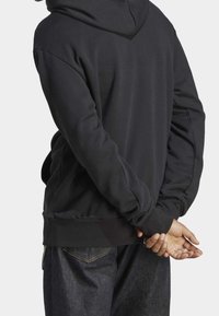 Svart huvtröja med avslappnad passform, med ribbade ärmslut och nederkant. Materialet verkar mjukt och har en slät struktur.