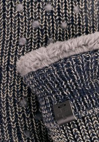 Gebreide marineblauwe en crème stof met een pluizige grijze voering. Bevat een zwart label met een kruis symbool. Zachte textuur en dik ontwerp.