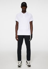 White polo shirt with short sleeves, paired with dark pants and black sneakers. A black cap with a logo and a black golf glove.