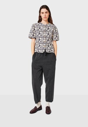 Kortärmad mönstrad blus i krämfärgad med marinblå geometriska mönster, tillsammans med löst sittande kolgrå byxor och bordeauxfärgade loafers.