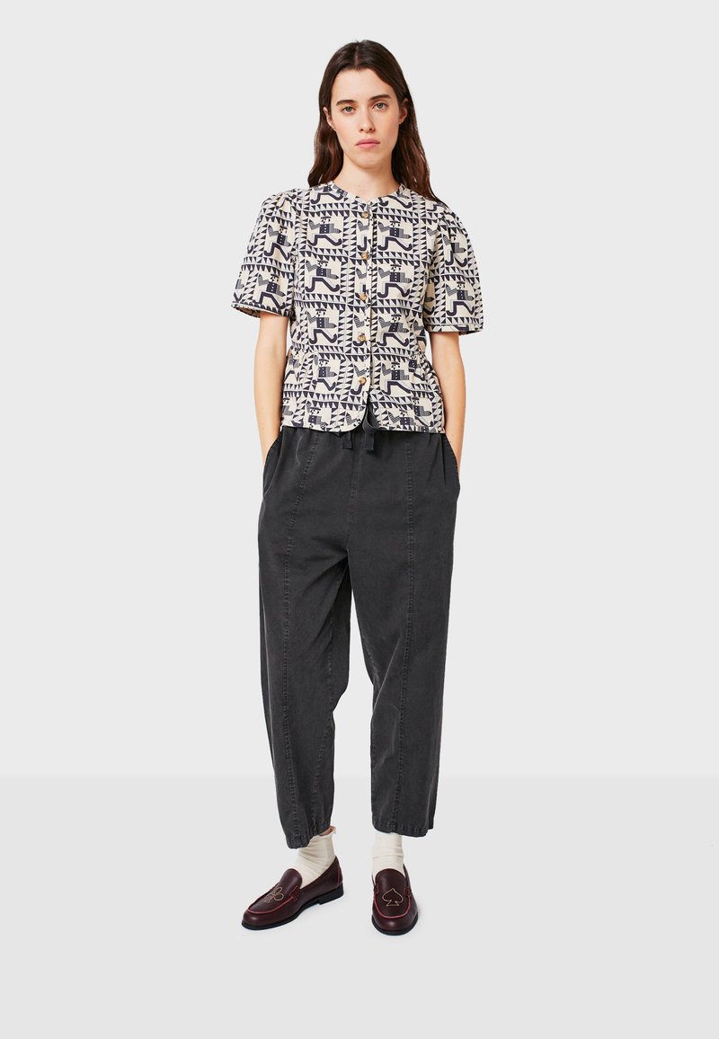 Geprint overhemd in crème en marineblauw, met geometrische patronen. Losse zwarte broek met taps toelopende enkels en bordeauxrode loafers.