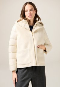 Giacca imbottita color crema con cappuccio, caratterizzata da una parte anteriore testurizzata, chiusura con cerniera e tasche laterali. Design leggero e casual.