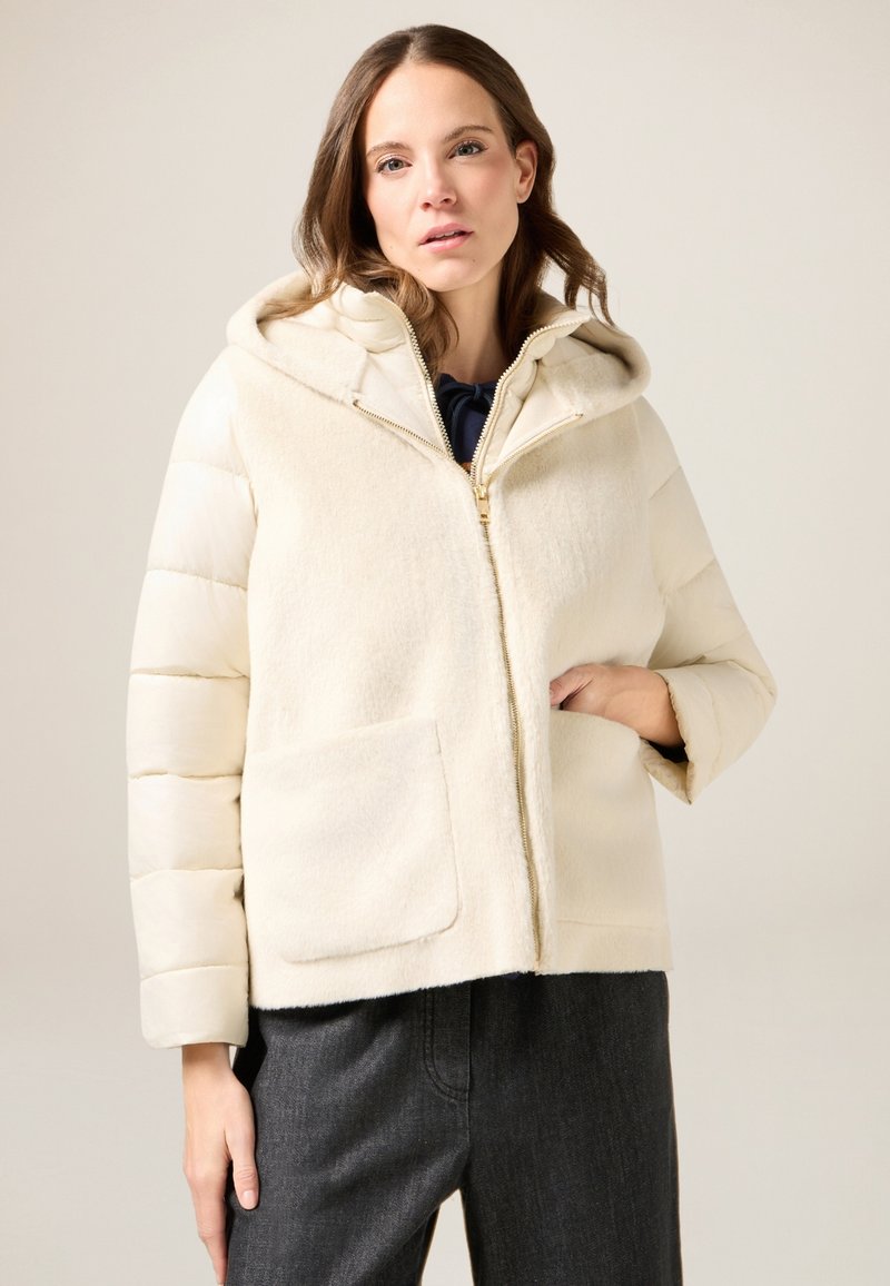Giacca imbottita color crema con cappuccio, caratterizzata da una parte anteriore testurizzata, chiusura con cerniera e tasche laterali. Design leggero e casual.