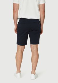 Bermuda biru navy yang terbuat dari katun dengan dua saku belakang, bagian depan datar, dan potongan yang disesuaikan. Dipadukan dengan sepatu sneakers putih dan kemeja lengan pendek.