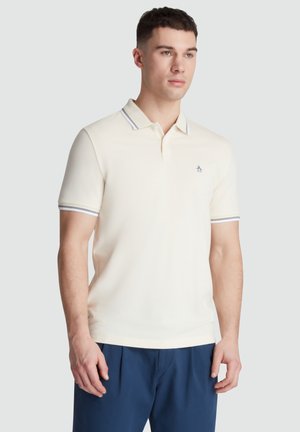 Crèmekleurig polo shirt met een kraag, voorzien van een marineblauw en wit gestreept accent op de kraag en mouwen. Inclusief een klein pinguïnlogo.