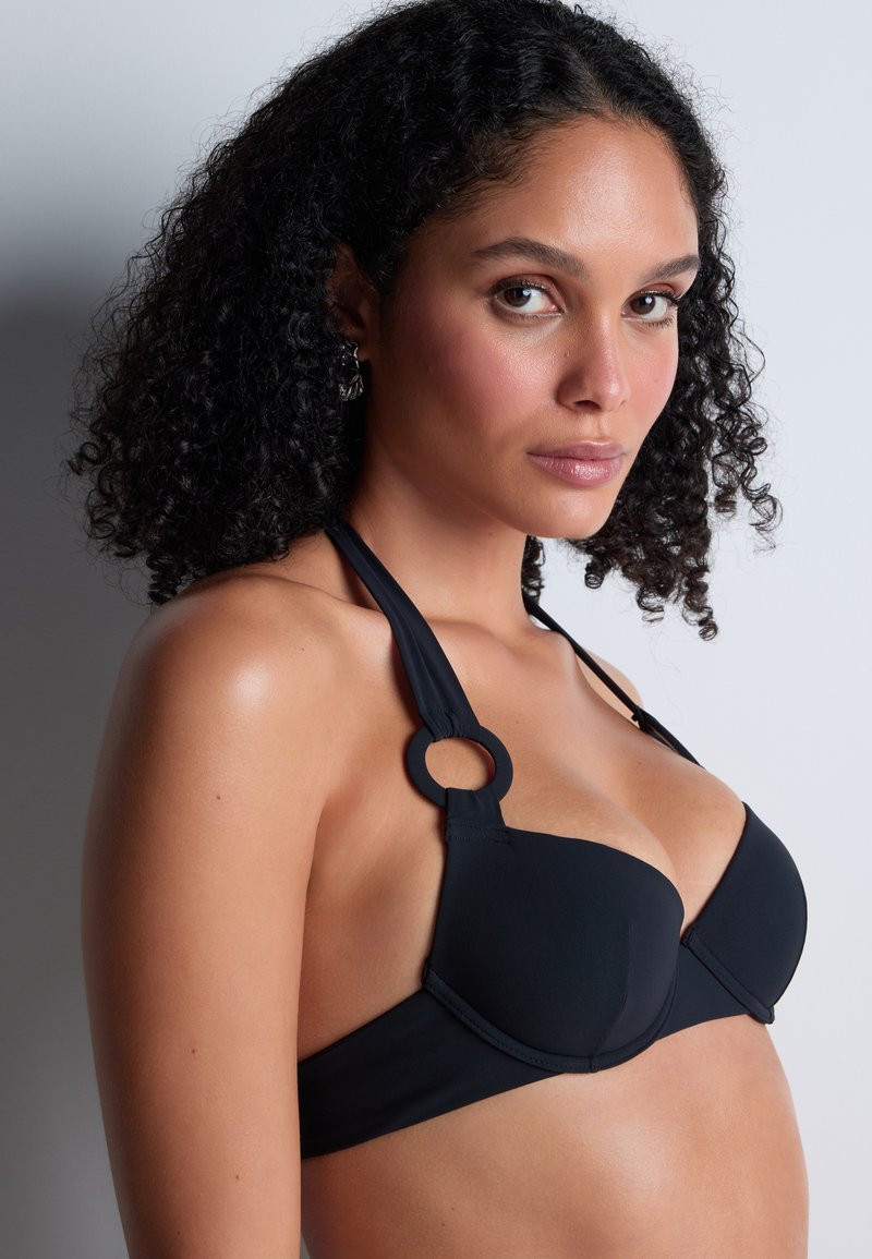 Haut de bikini noir avec des bonnets moulés et un design à col halter. Présente un accent en métal circulaire à l'épaule pour une touche de détail supplémentaire.