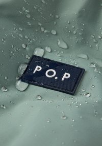 Waterdruppels op groene waterdichte stof met een donkerblauw rechthoekig label met de tekst "P.O.P." in witte letters.