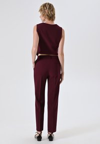 Top senza maniche corto color bordeaux abbinato a pantaloni a vita alta coordinati, caratterizzati da una texture liscia e un design minimalista.