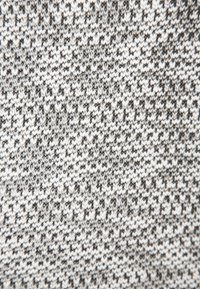Stickad tyg med ett texturerat mönster i svart och vitt. Har växlande mörka och ljusa garn i små upprepande former.