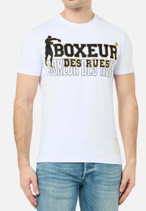 Mann trägt weißes T-Shirt mit schwarzem und goldenem Schriftzug "Boxeur Des Rues" und Silhouettengrafik, kombiniert mit hellblauen Jeans.