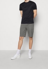 Námořnické tričko s kulatým výstřihem a embosovaným logem, spárované se šedými šortkami. Model má na sobě bílé tenisky a bílé ponožky do kotníků.