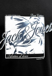 Czarna tkanina z białym i niebieskim abstrakcyjnym wzorem liści oraz tekstem „Jack & Jones”, „Raw Cotton” i „Definition of denim.”