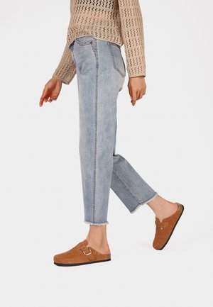 Jeans a gamba dritta blu chiaro con orli sfrangiati, abbinati a mocassini in suede marrone con dettaglio di fibbia laterale.