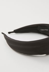 Black fabric headband with a smooth texture, featuring a minimalistic design and a Calvin Klein logo tag on one side.