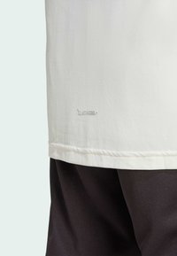 Weißes T-Shirt mit "CLIMACOOL+"-Logo in einem dezenten Grau am Saum. Weicher Stoff und lockere Passform, kombiniert mit schwarzen Shorts.
