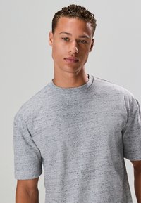 Grijs T-shirt met korte mouwen van een zachte, gestructureerde stof met een subtiel gespikkeld patroon. Met een ronde hals en aangesloten pasvorm bij de schouders.