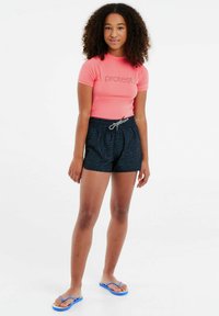 Rash guard in helderroze met "protest" logo, gecombineerd met marineblauwe shorts met een zwart zebrapatroon en blauwe slippers.