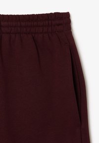 Bordeaux joggingbroek met een elastische tailleband, zijzakken en een zachte textuur. De stof heeft een gladde, consistente tint.
