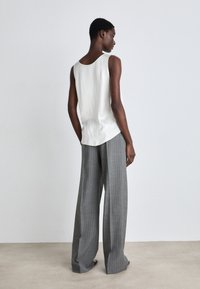 Valkoinen hihaton paita, jossa on pyöreä kaula-aukko, yhdistettynä leveälahkeisiin harmaisiin raidallisiin housuihin. Tasainen tekstuuri, minimalistinen muotoilu.