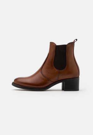 Brauner Leder-Stiefelette mit schwarzem elastischem Seitenteil, Blockabsatz und Zuglasche, auf weißem Hintergrund, Seitenansicht.