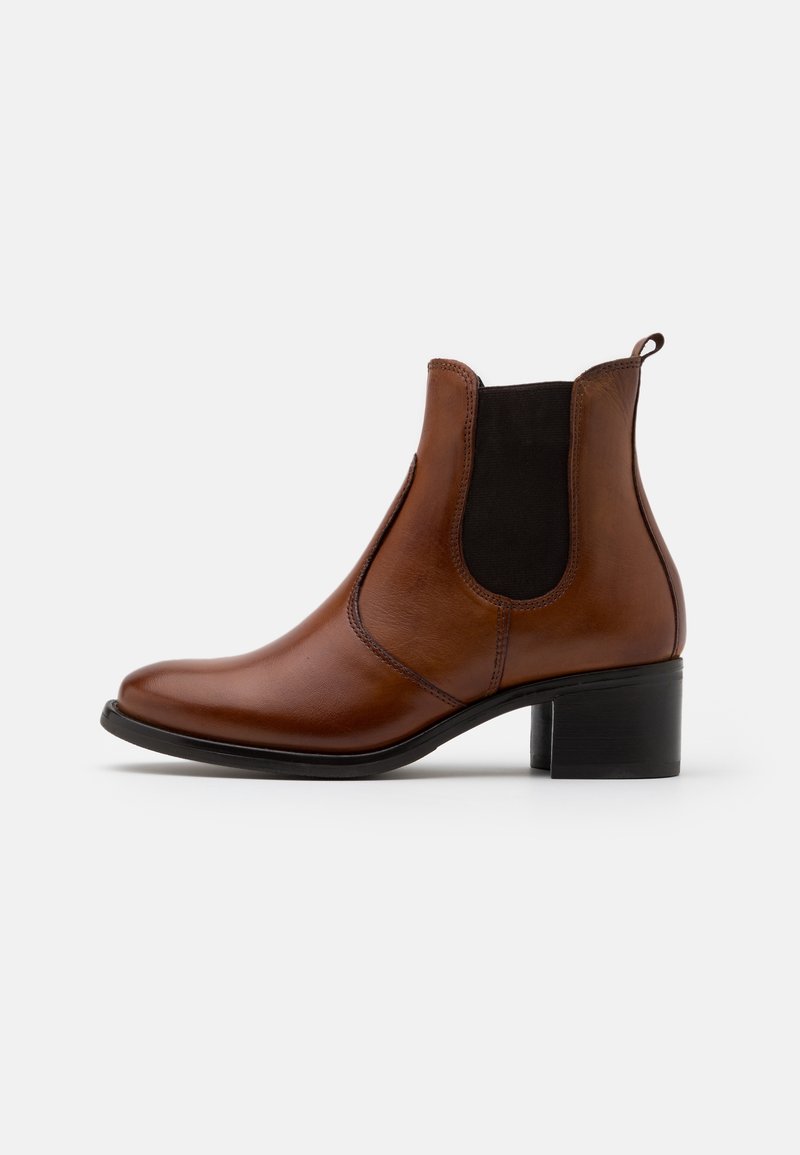 Bottine en cuir marron avec un panneau latéral élastique noir, talon bloc et tirette, présentée sur fond blanc, vue de profil.