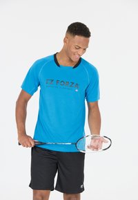Blå sporttröja med korta ärmar och svarta detaljer, med logotypen "FZ FORZA" på framsidan. Svarta shorts och en badmintonracket.