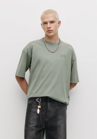 Tricou scurt de culoare verde deschis, cu guler circular și un logo subtil. Potrivit cu blugi din denim închis, cu accesorii decorative.