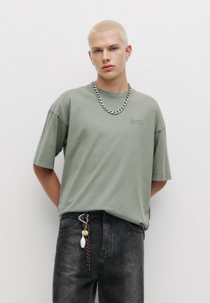 Lys grøn kortærmet t-shirt med rund hals og subtilt logo. Sammen med mørke denim jeans med dekorativt hardware og accessories.