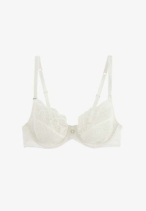 Reggiseno bianco con ferretto in pizzo, spalline regolabili e un piccolo ciondolo circolare dorato al centro davanti su uno sfondo semplice.