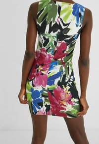 Vrouw in een mouwloze, aansluitende mini-jurk met gedurfde abstracte bloemenpatronen in rood, blauw, groen, zwart en witte kleuren.