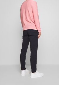 Jasnoróżowa koszula z długim rękawem i okrągłym dekoltem, zestawiona z dopasowanymi ciemnymi spodniami i białymi sportowymi butami. Gładka tkanina, prosty fason.