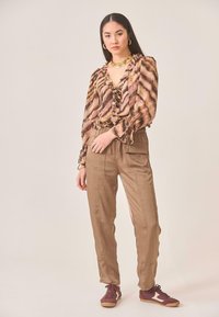 Blusa estampada en marrón y beige con volantes, combinada con pantalones marrones claros con bolsillos laterales, llevada con zapatillas burdeos.