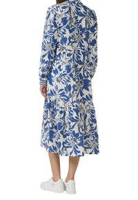 Blumenkleid mit blauen und weißen Farben, langen Ärmeln, einer taillierten Taille und einem gestuften Rock. Kombiniert mit weißen Sneakers.