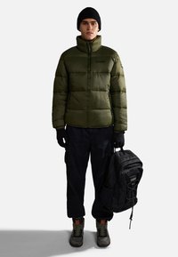 Giacca a vento verde oliva, guanti neri, pantaloni cargo neri larghi, berretto nero, stivali robusti grigio-verdi e uno zaino nero.