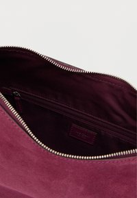 Intérieur d'un sac en daim bordeaux avec une doublure foncée et une poche zippée. Fermeture éclair en argent offrant un détail fonctionnel. Texture lisse.