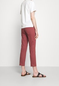 Witte katoenen t-shirt met korte mouwen, gecombineerd met bordeaux cropped pants. Zwarte sandalen hebben een platte zool en twee bandjes over de voet.