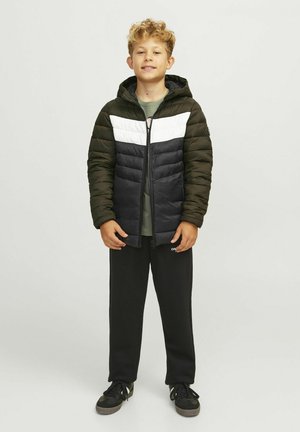 Veste matelassée en vert foncé, noir et blanc avec fermeture éclair, dotée d'une capuche et d'un matelassage horizontal. Associée à un pantalon de survêtement noir et des chaussures.