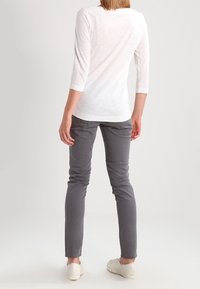 Weißes Oberteil mit drei Viertelärmeln, graue schmale Hose und helle Schuhe. Lässiges Outfit mit schlichtem Design und weicher Textur, von hinten betrachtet.
