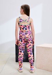 Ensemble de vêtements de sport comprenant un crop top multicolore à motif floral avec un dos découpé et un legging assorti au design similaire avec une taille haute.