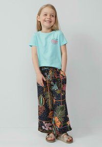 Lichtblauwe katoen t-shirt met een watermeloenafbeelding en een relaxte pasvorm, marineblauwe gebloemde broek met kleurrijke flora. Platte sandalen maken de outfit compleet.