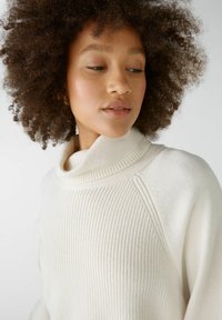 Cremfarbener gerippter Rollkragenpullover mit einer weichen Textur, ausgestattet mit einem hohen Kragen und Raglanärmeln für eine lässige Passform.