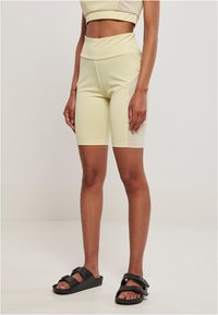 Shorts da ciclismo a vita alta di colore giallo chiaro, realizzati in materiale elastico, con una consistenza liscia e un dettaglio a pannello laterale. Indossati con sandali neri.